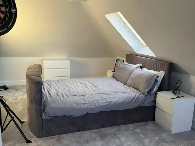 Loft bedroom with a grey upholstered bed, white bedside drawers and a roof window set into the sloping ceiling