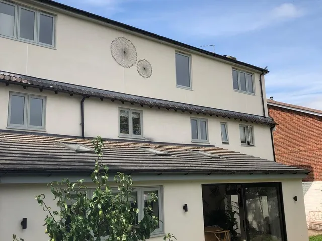 White-rendered house with a full-width rear dormer, grey windows and a single-storey extension with sliding doors, seen from the garden