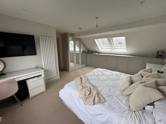 Loft bedroom with a wall-mounted TV above a dressing table, a tall white radiator, mirrored wardrobes and eaves cupboards beneath roof windows