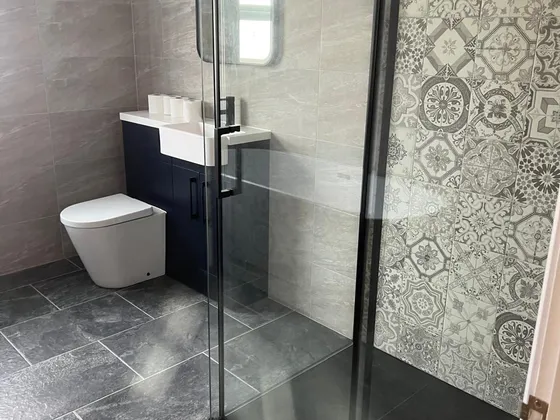 Shower room with a black-framed walk-in shower, patterned grey feature tiles, stone-effect wall tiles, dark slate-effect floor tiles and a navy vanity unit