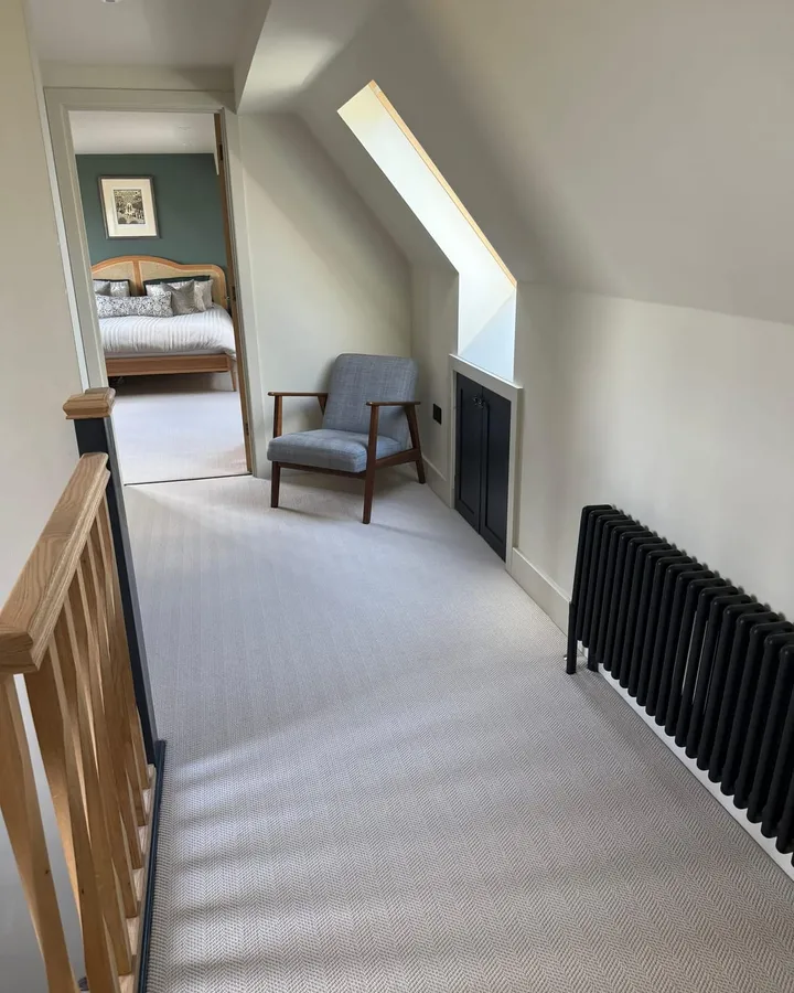 Loft landing with a grey armchair under a roof window, black eaves cupboard doors and radiator, and an open door to a bedroom with a green feature wall