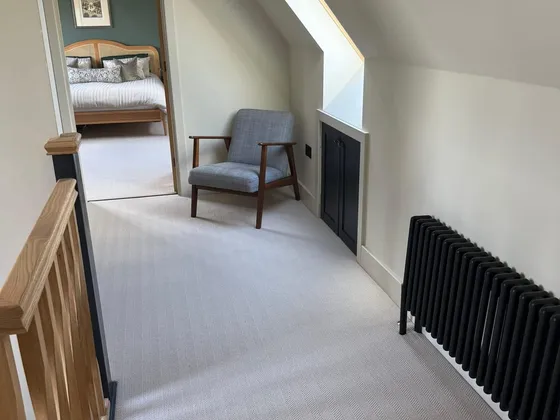 Loft landing with a grey armchair under a roof window, black eaves cupboard doors and radiator, and an open door to a bedroom with a green feature wall